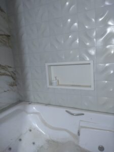 Banheiro com revestimento 3D, nicho embutido e banheira instalada durante reforma.